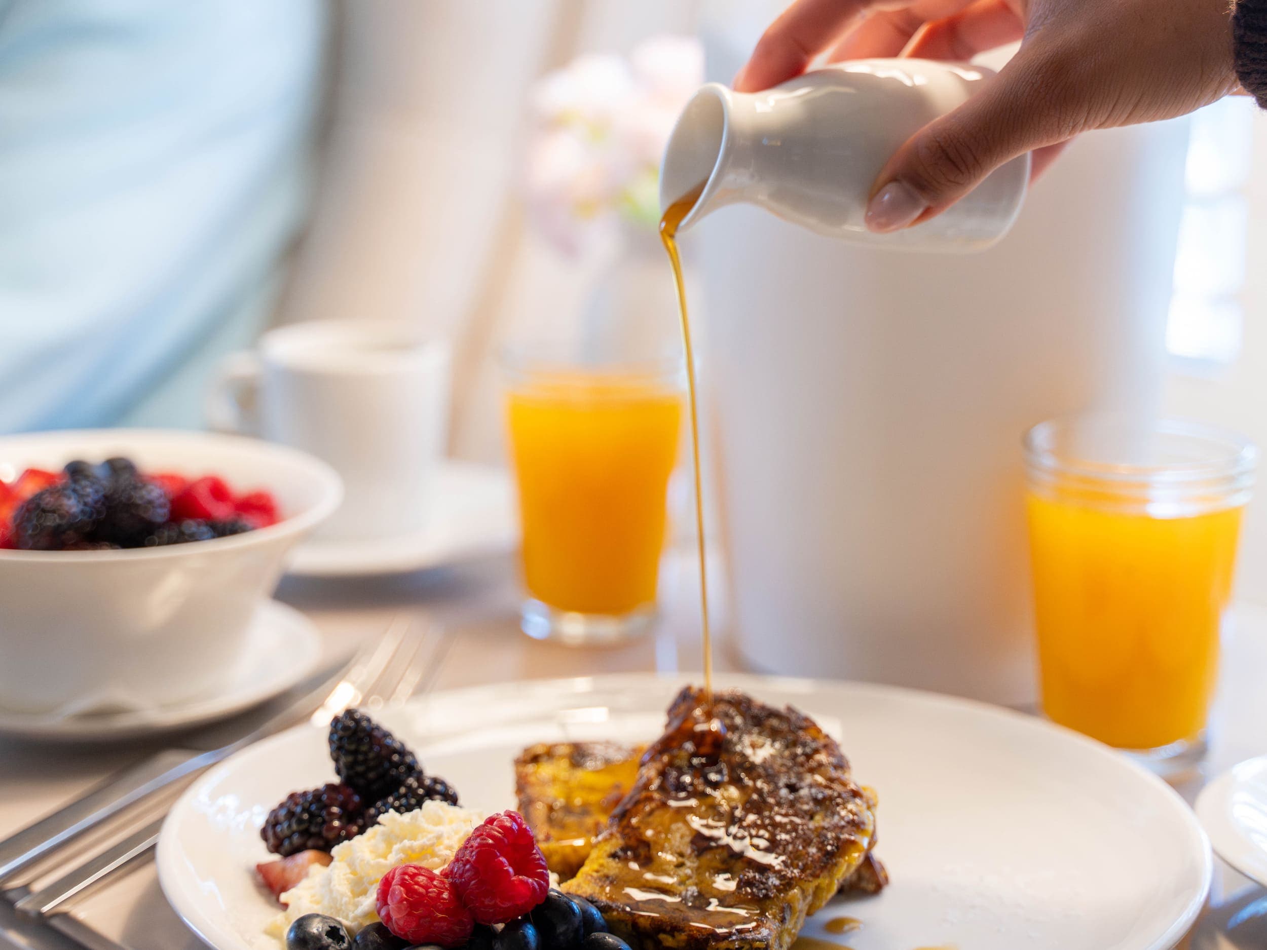 A guest pouring syrup over french toast and berries at the Chatham Inn