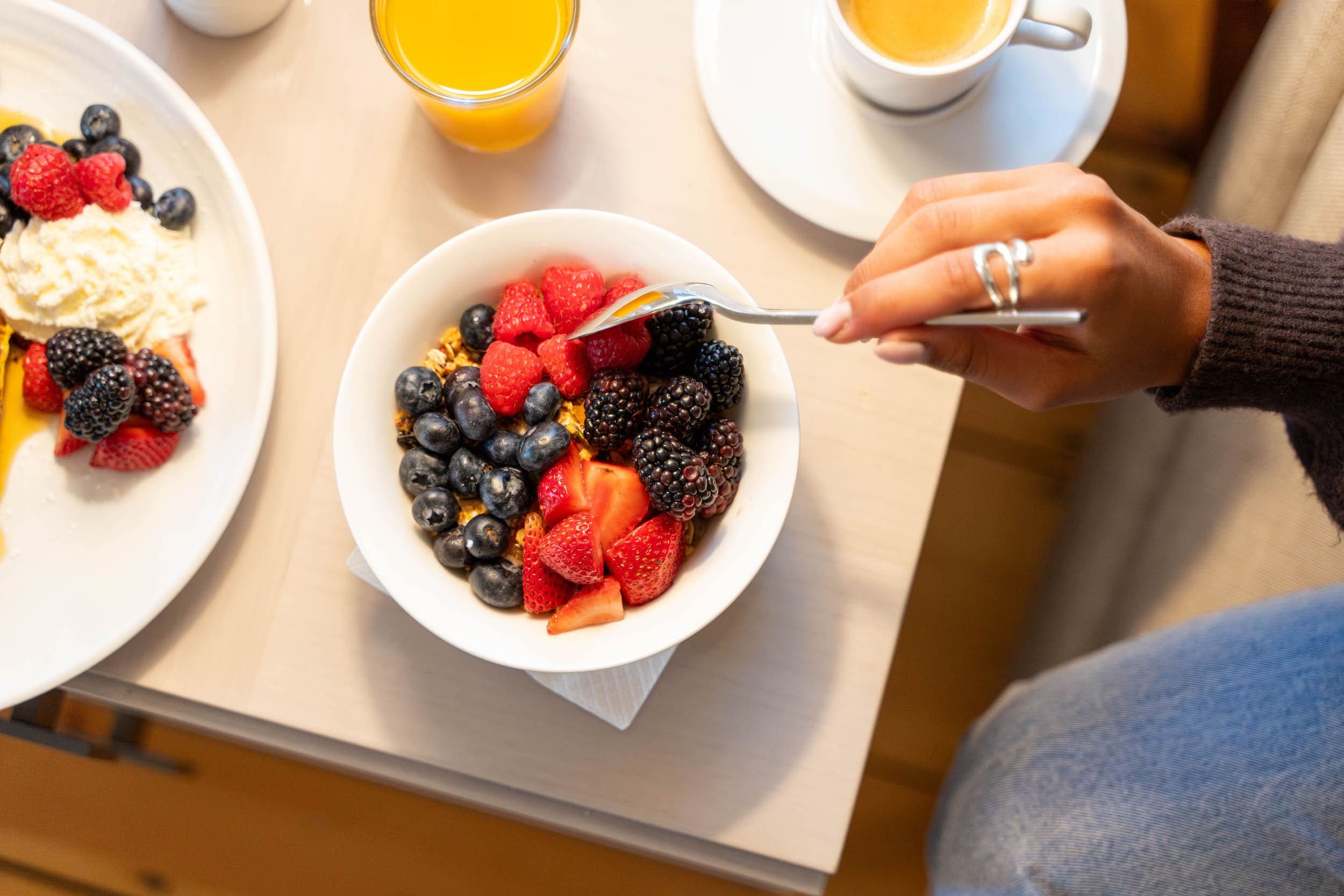 A bowl of yogurt, granola, mixed berries, coffee, and orange juice in a room at the Chatham Inn