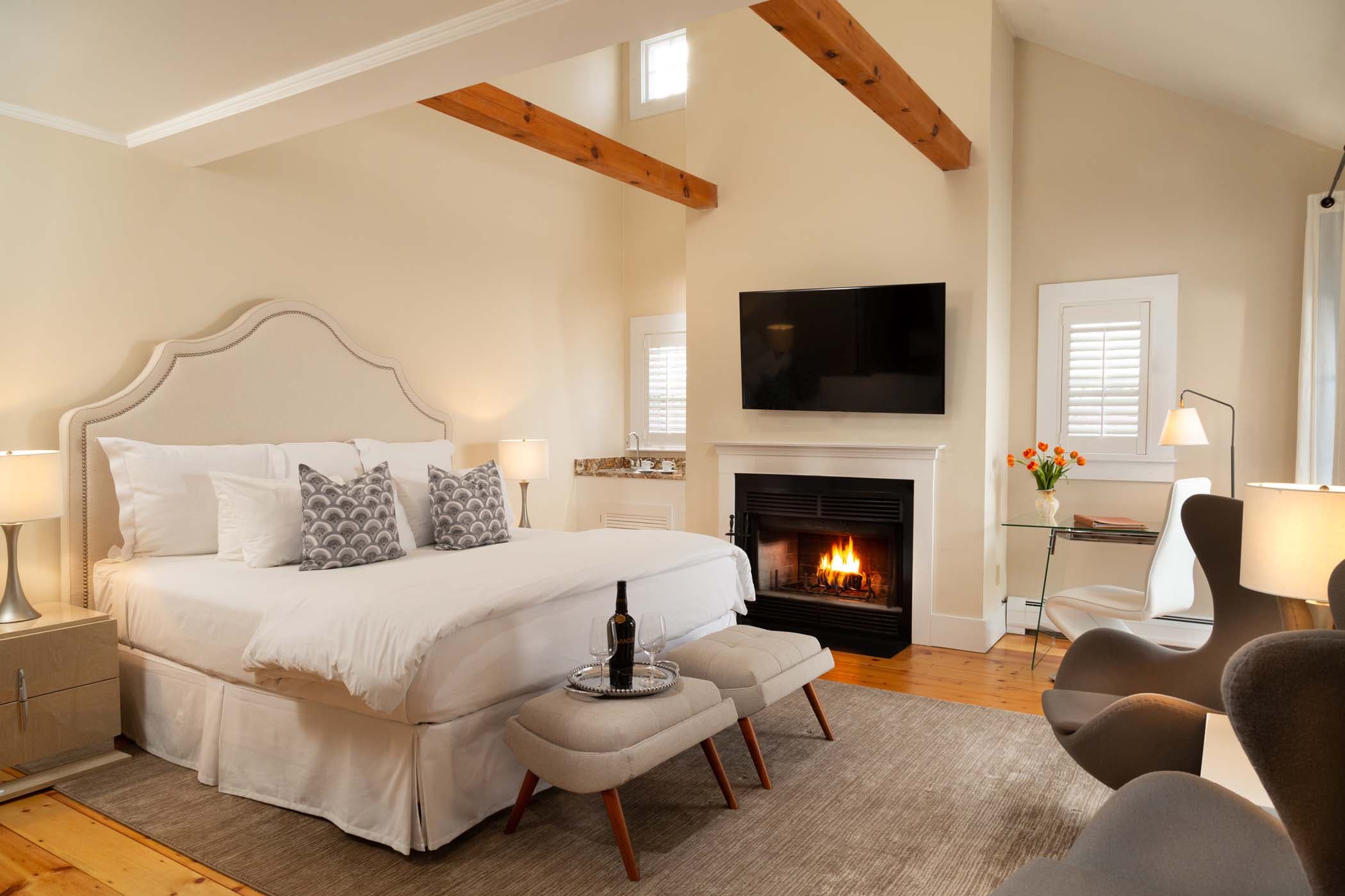 A large bed with exposed wood beams above it, a fireplace, Tv, and sitting area in Room 12 at Chatham Inn