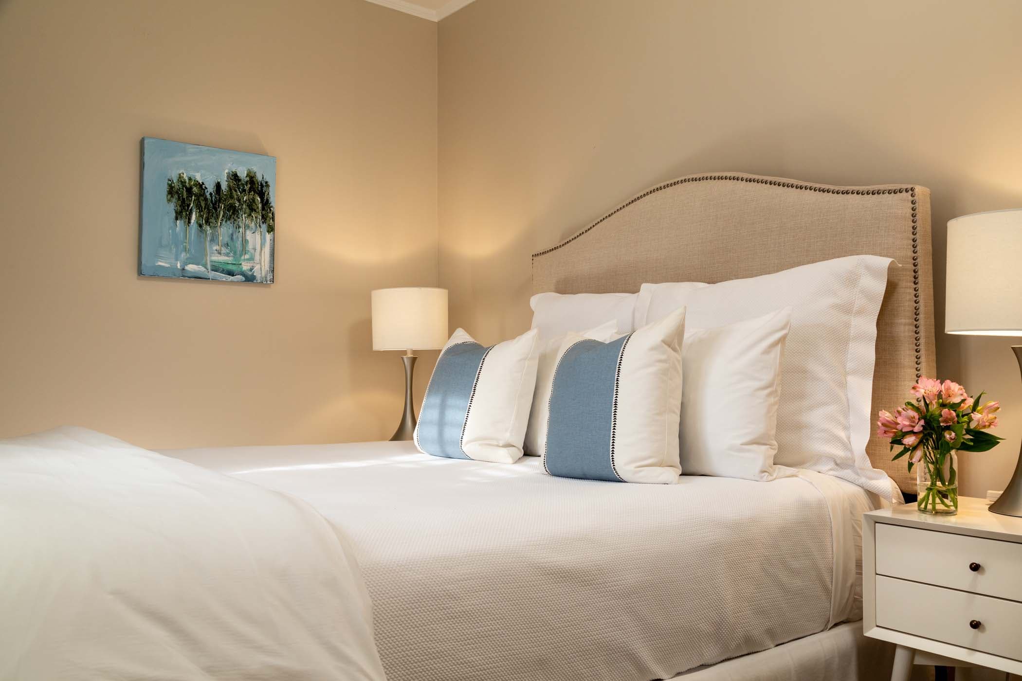 A queen bed, wall art, and a side table with a bouquet of pinks flowers in Room 14 at Chatham Inn