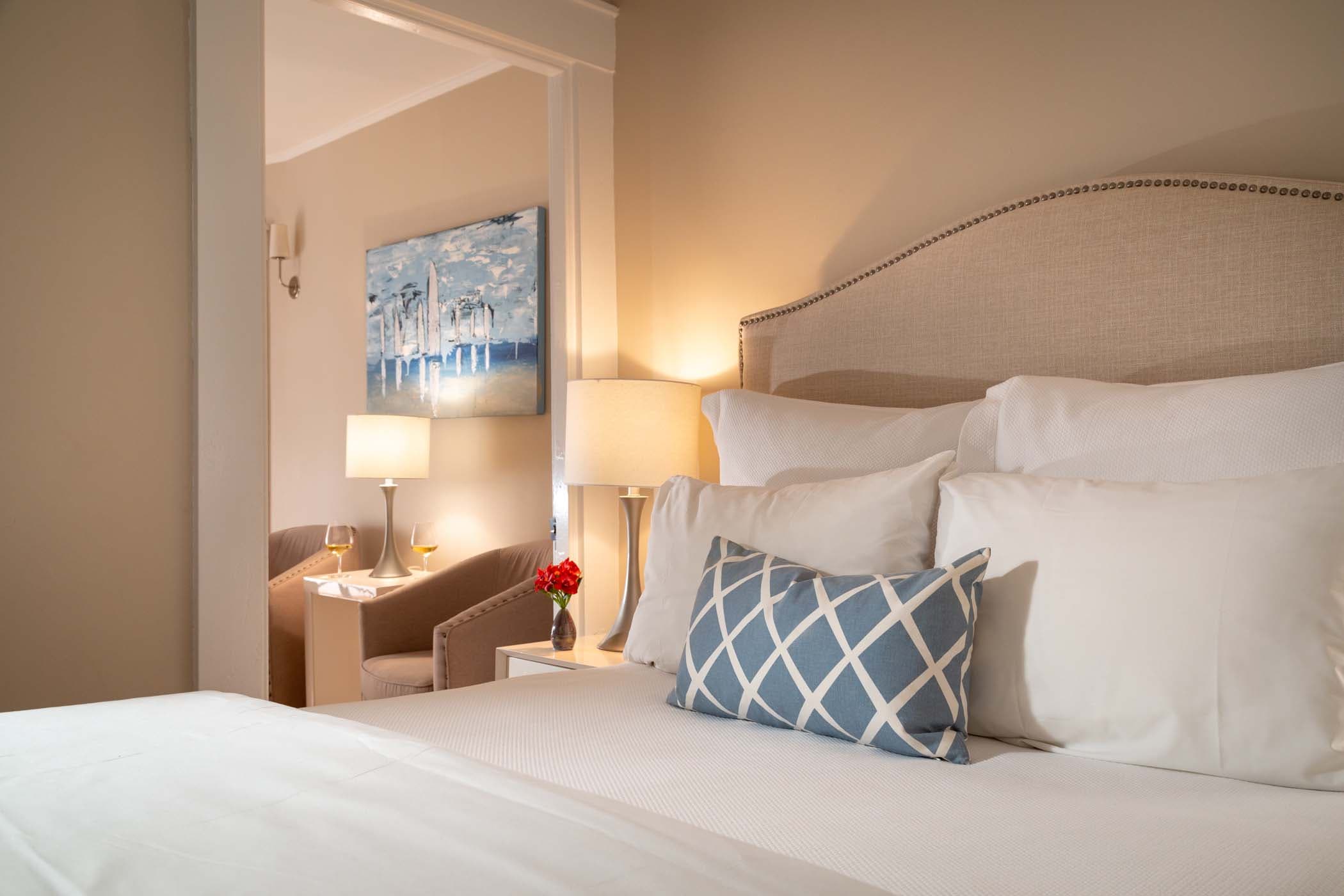 A queen bed, a side table with red flowers, and two lounge chars in Room 15 at Chatham Inn