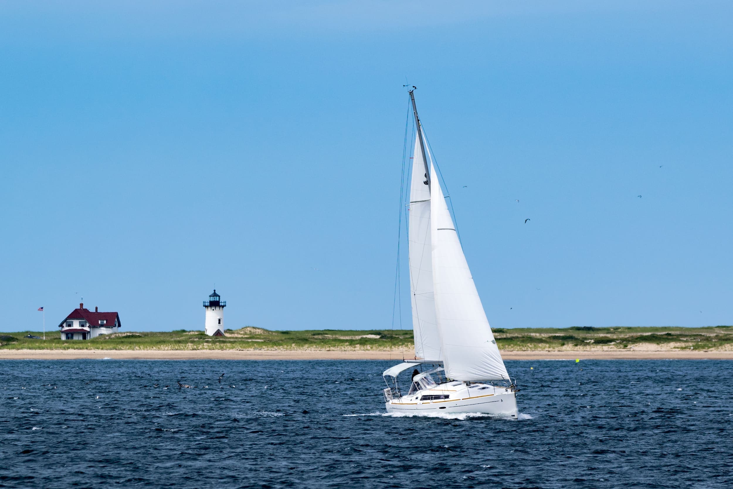 A sailboat in the water with a lighthouse on teh shoreline