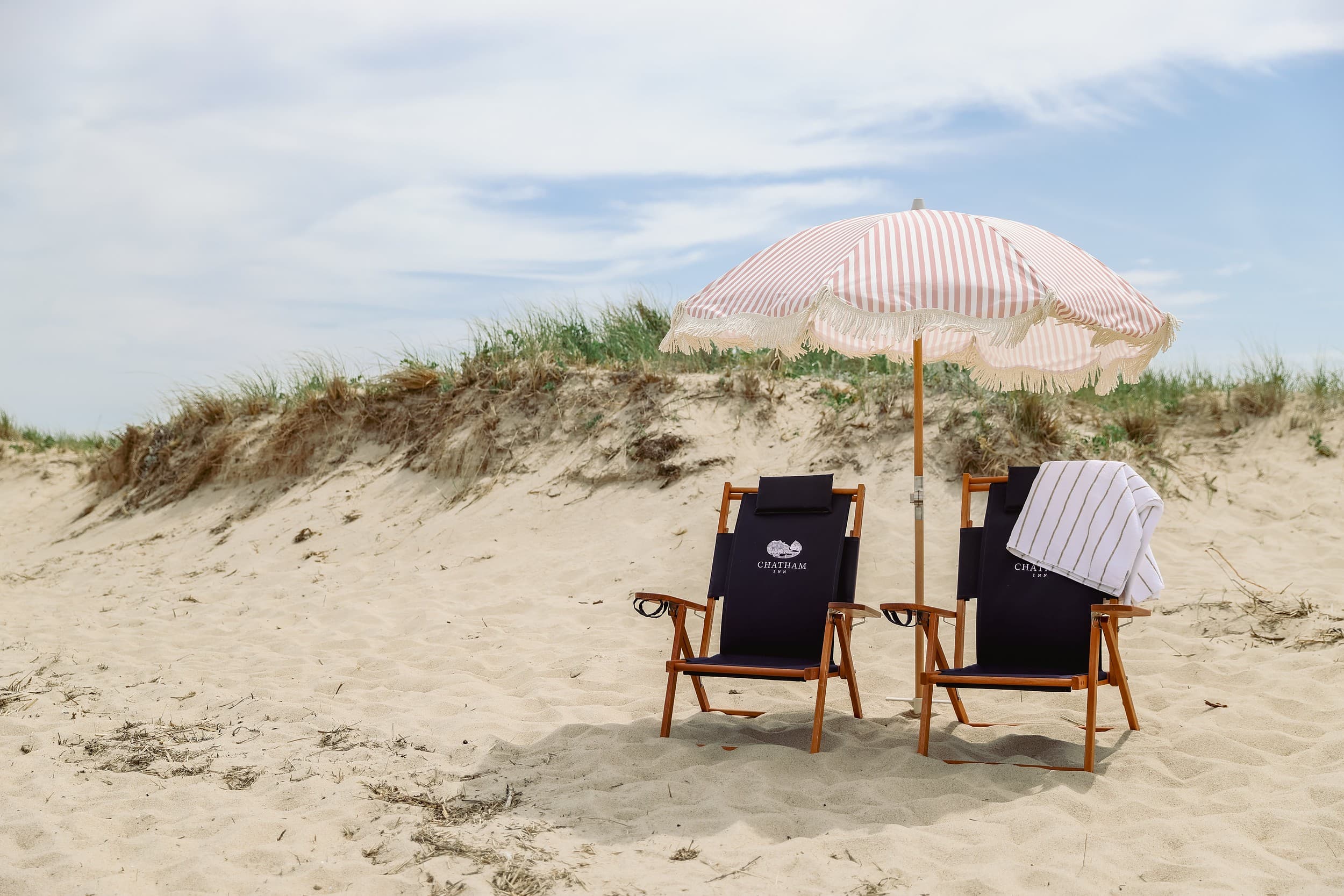 Branded Chatham Inn beach chairs and a striped umbrella on the dunes, a coastal escape in Chatham, Massachusetts on Cape Cod.