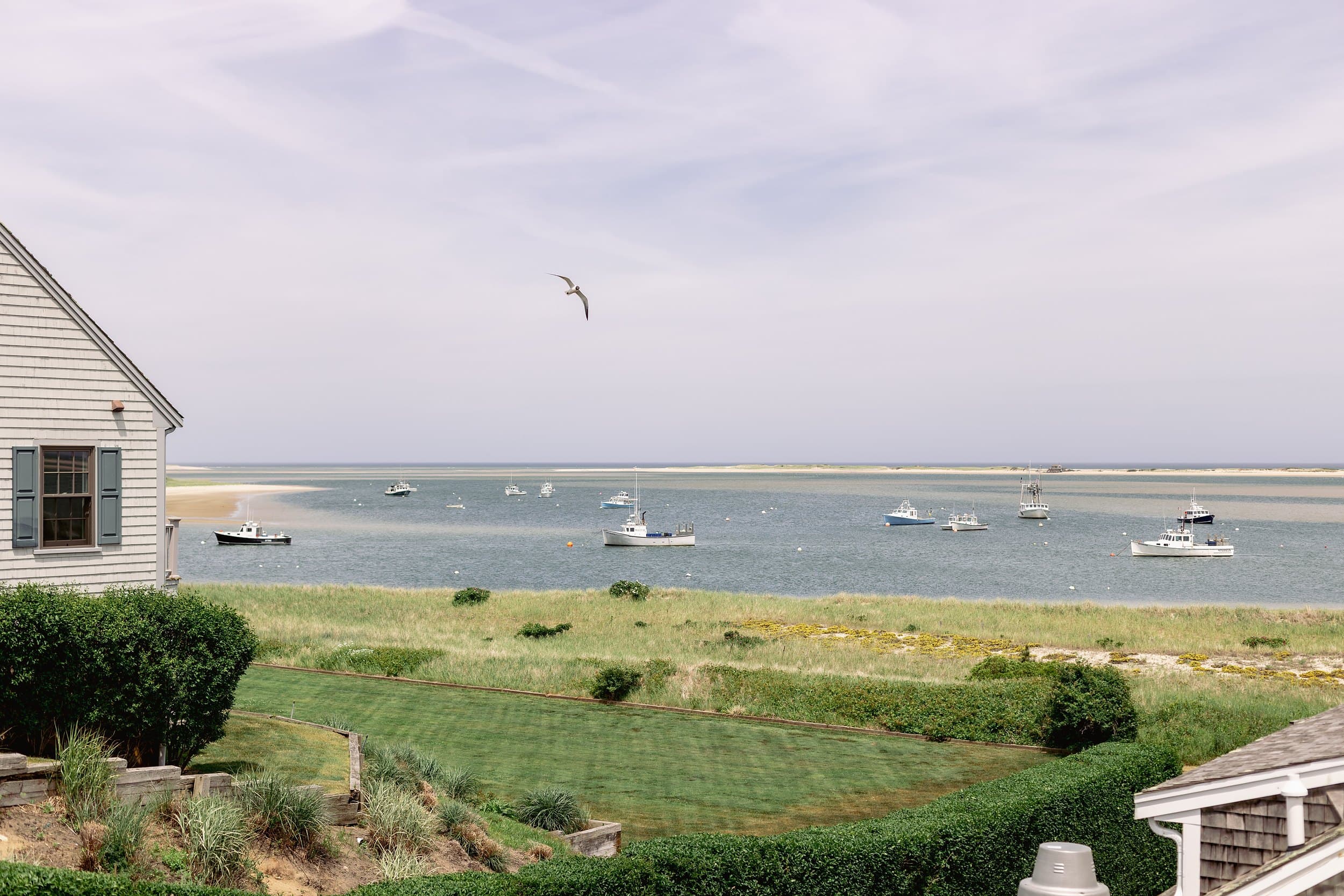 Fishing boats moored in Chatham Harbor with a shingled cottage and seagull, a classic Cape Cod view near Chatham Inn, Massachusetts.