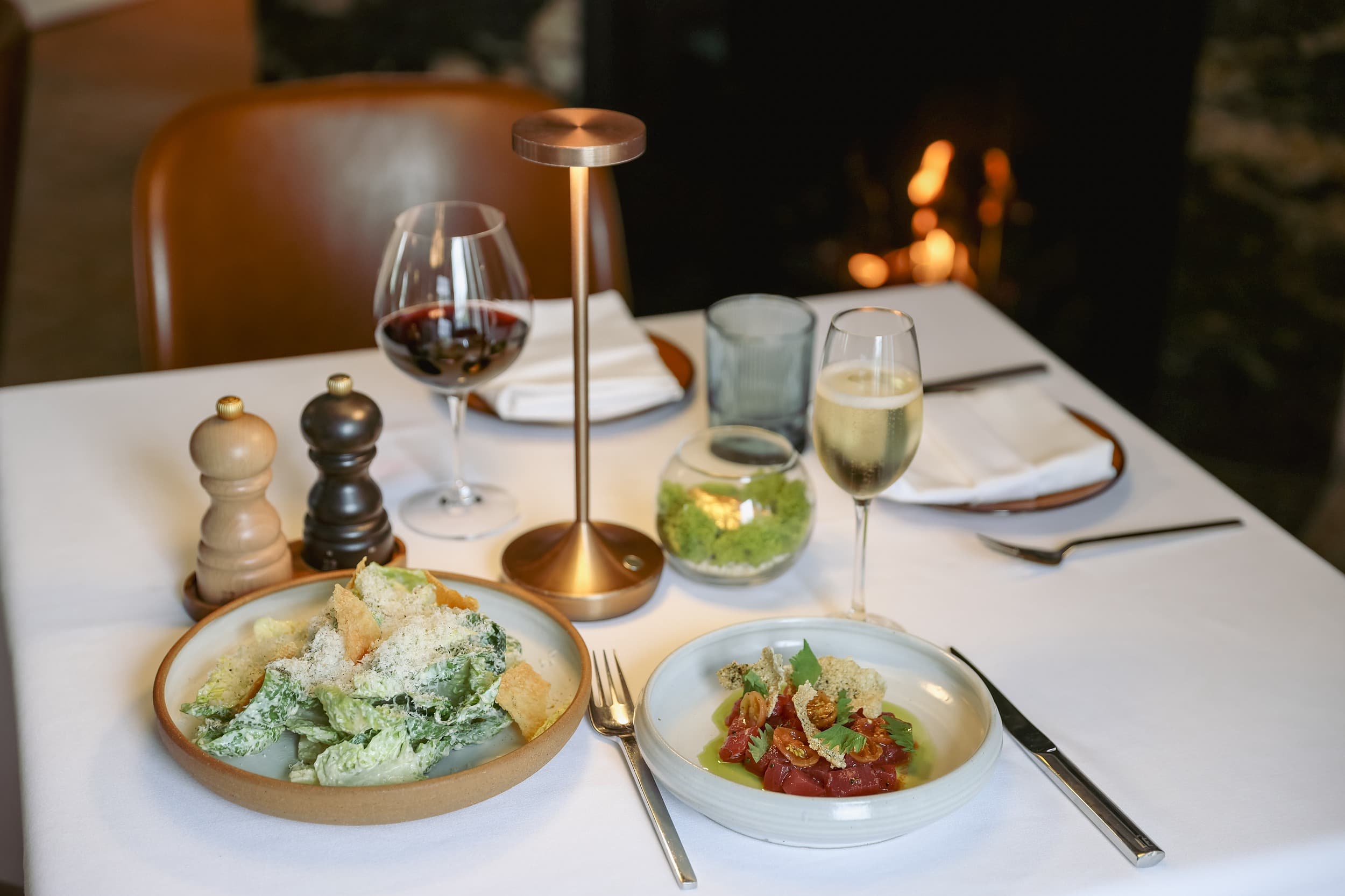 Caesar salad and tuna tartare paired with red and sparkling wine beside the fireplace at Chatham Inn's fine-dining restaurant on Cape Cod.