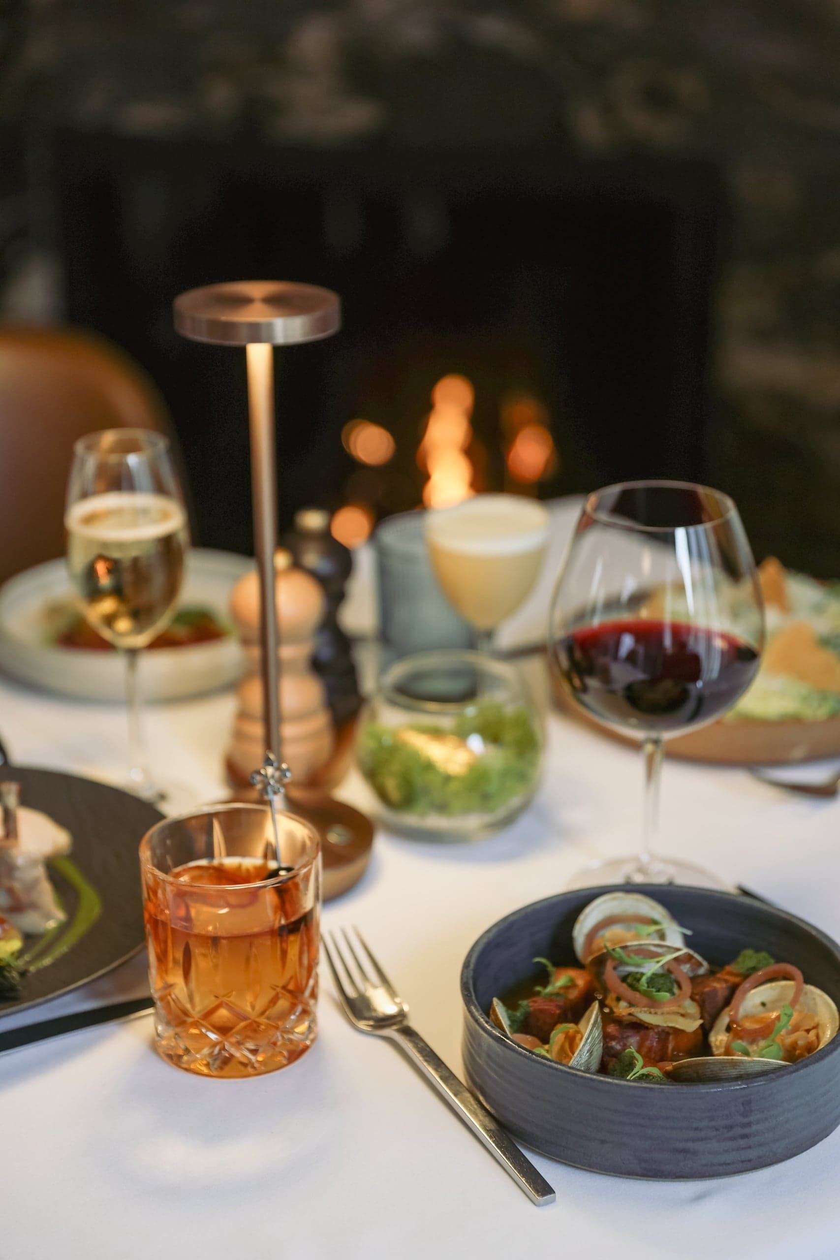 Seasonal seafood entrée with a craft cocktail and red wine by the fire at Chatham Inn's restaurant in Chatham, Massachusetts.